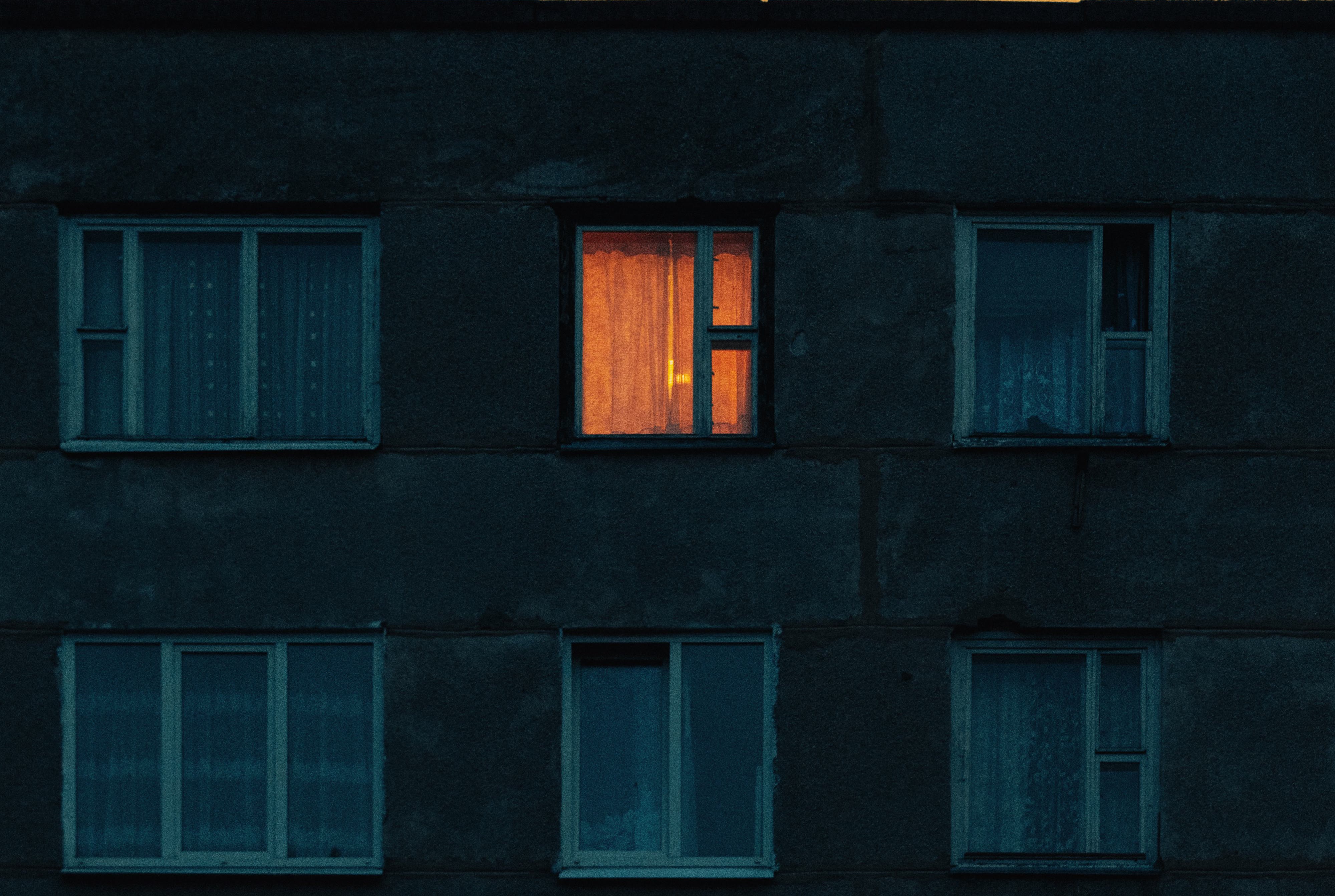 A block of flats at dawn with one warm lit window